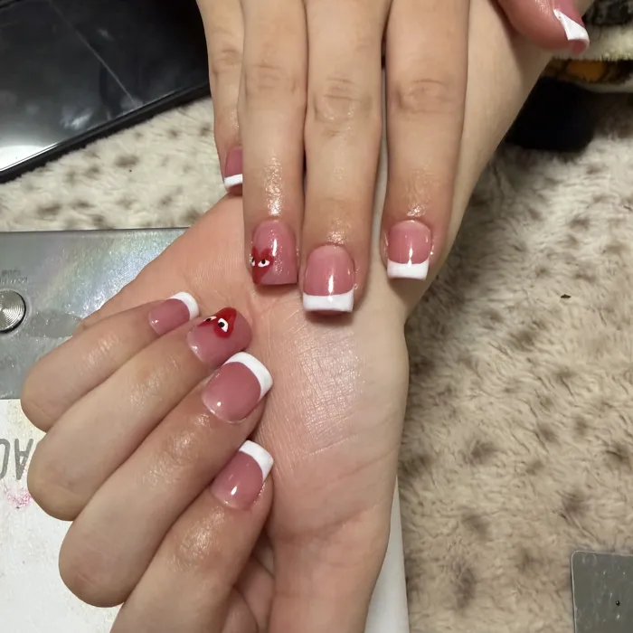 Classic white French tips with hand-painted cherry red heart accent nails
